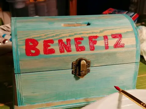 eine blau bemalte Holztruhe mit roten der Aufschrift "Benefiz"